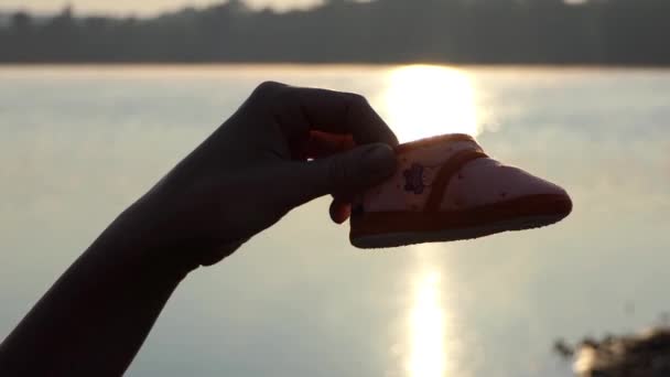 Το χέρι του μπαμπά μια παίζει με παντόφλες του μωρού σε μια τράπεζα στη λίμνη στο ηλιοβασίλεμα — Αρχείο Βίντεο