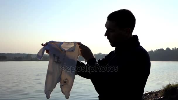 El joven padre sonríe con un traje de mameluco para su bebé al atardecer espléndido — Vídeos de Stock