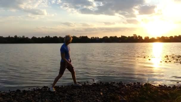 Atardecer brillante y un niño arrojando piedra plana en el agua del río en 4k — Vídeos de Stock