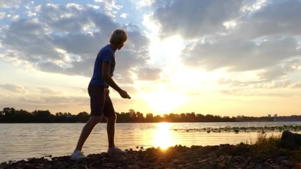 Magisk solnedgång och en pojke platt sten i floden bevattnar i 4k — Stockvideo