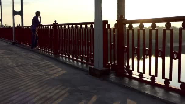 Le jeune homme regarde la rivière Dnipro, sourit et pense sur un pont — Video