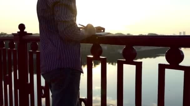 Talentovaný muž udeří myšlenky a položí je v notepadu na mostě — Stock video