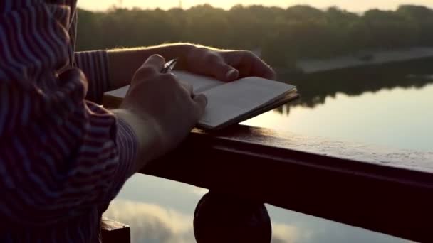 Mãos masculinas colocam um pouco para baixo em uma ponte do rio no por do sol — Vídeo de Stock