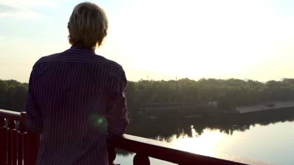 Happy Man chasquea los dedos en un puente sobre el Dnipro al atardecer en Slo-Mo — Vídeos de Stock