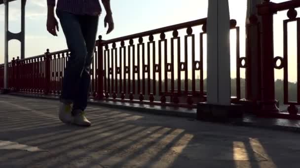 Αρσενικό πόδια με τα πόδια καιρό μια σύγχρονη γέφυρα σε ένα υπέροχο ηλιοβασίλεμα το καλοκαίρι σε αργή κίνηση — Αρχείο Βίντεο