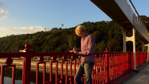 Getalenteerd Man staat en zijn ideeën legt op een rivier brug bij zonsondergang in Slo-Mo — Stockvideo