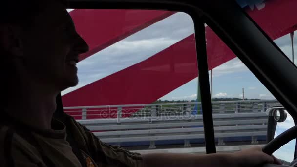Um homem dirige um carro enquanto vai em uma ponte vermelha no verão — Vídeo de Stock