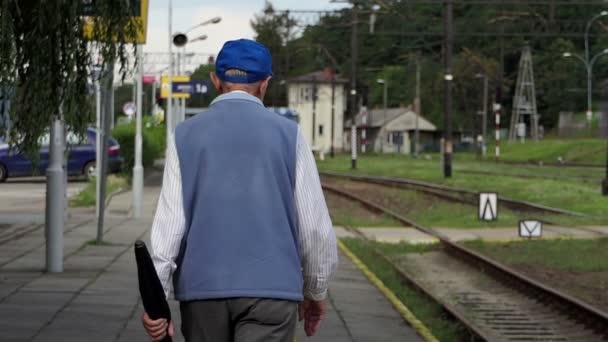 Старий чоловік в куртці йде по залізниці влітку в шлю-мо — стокове відео