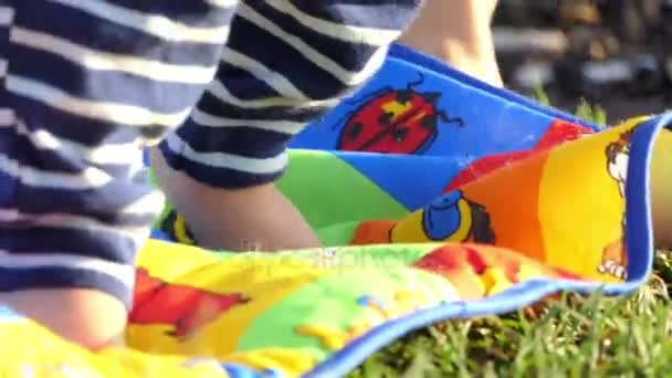 Los pies del bebé van en una cubierta multicolor colocada en un césped verde — Vídeo de stock