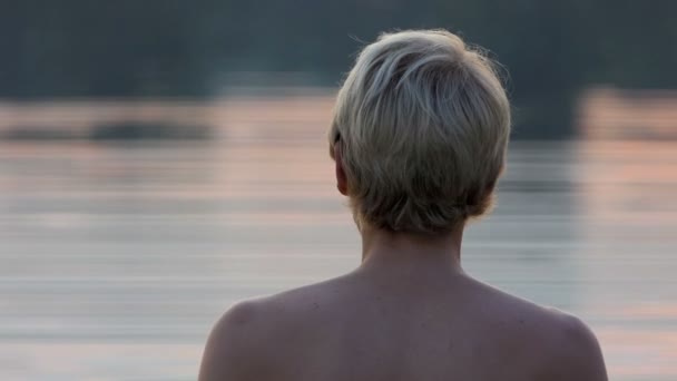 Νεαρός στέκεται στα νερά της λίμνης, πυροβόλησε από πίσω ένα υπέροχο ηλιοβασίλεμα στο Slo-Mo — Αρχείο Βίντεο