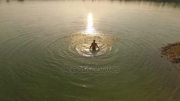 Ένας νεαρός άνδρας ρίχνει νερό επάνω με τα χέρια του σε μια λίμνη στο ηλιοβασίλεμα σε slo-mo — Αρχείο Βίντεο
