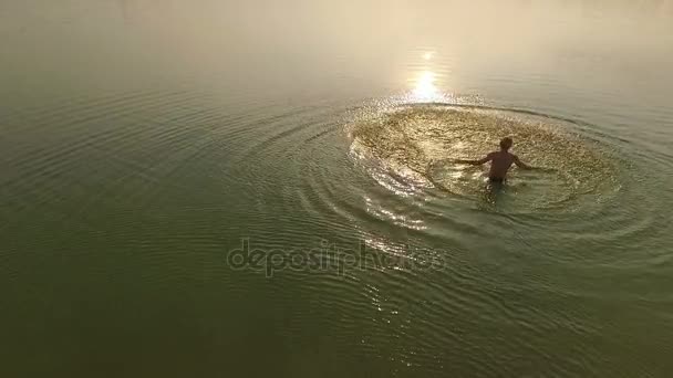 Un hombre feliz arroja agua con sus manos en un lago al atardecer en slo-mo — Vídeos de Stock