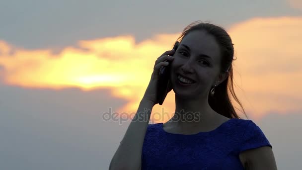 Une jeune femme sourit et appelle quelqu'un par son smartphone au coucher du soleil — Video