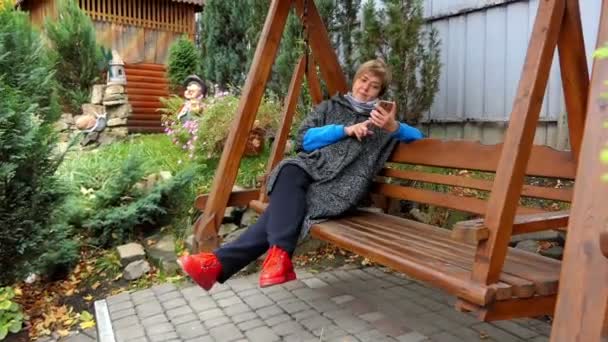 En leende kvinna i moderiktiga kläder gungar på en bänk — Stockvideo
