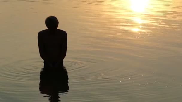 El hombre se para en un río, levanta el agua en las manos. se cae en Aunset — Vídeos de Stock