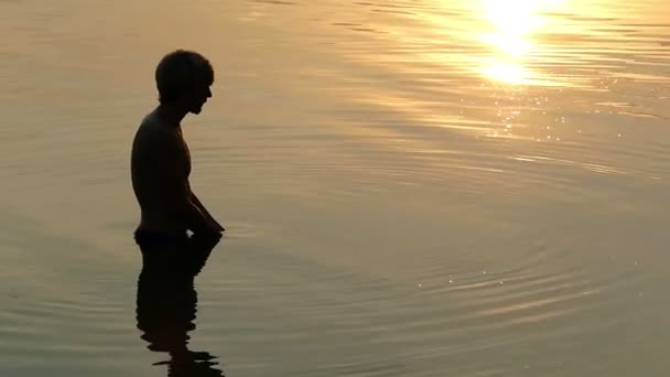 El joven levanta el agua del río en las palmas y hace una señal de amor al atardecer — Vídeos de Stock