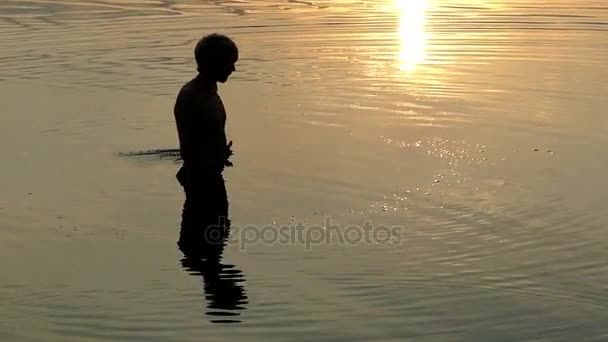 Молодой человек кружит в речных водах и смотрит на закат — стоковое видео