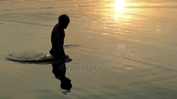 Junger Mann dreht bei Sonnenuntergang einen großen Kreis um sich im Wasser — Stockvideo