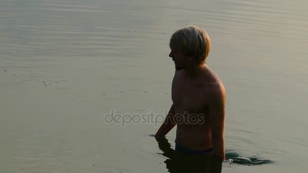 Блондин людина річка піднімає воду в на долоні і кидає його вгору на заході сонця в Slo-Mo — стокове відео