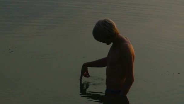 Man Stands in River Water. Seus dedos vão para a superfície ao pôr do sol — Vídeo de Stock