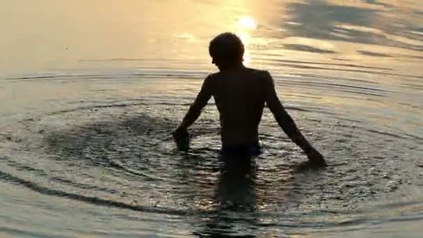 Arty άνθρωπος κάνει έναν μεγάλο κύκλο γύρω από τον εαυτό του στο νερό στο ηλιοβασίλεμα — Αρχείο Βίντεο