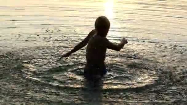 Junger Mann dreht bei Sonnenuntergang schnell einen Kreis um sich selbst im Wasser — Stockvideo