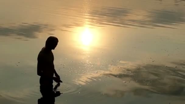 Loira homem fica no rio água e joga um plana cascalho no por do sol — Vídeo de Stock