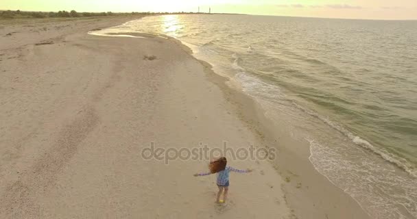 4k aérea - Hermosa chica se da la vuelta en una playa de arena al atardecer — Vídeo de stock