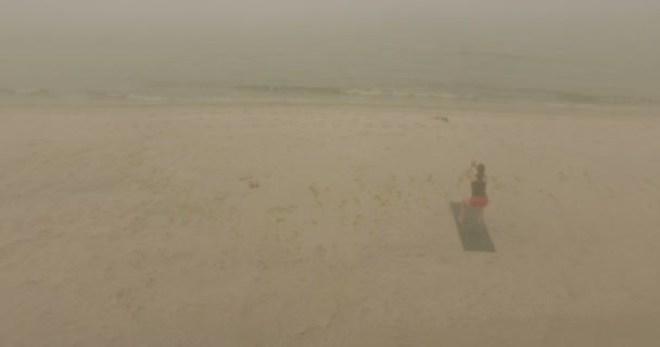 苗条的女人站在瑜伽垫和弯曲她的膝盖在沙滩上 — 图库视频影像