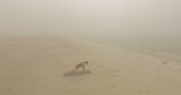 Hermosa chica estira sus piernas en una playa de arena en el tiempo brumoso . — Vídeo de stock