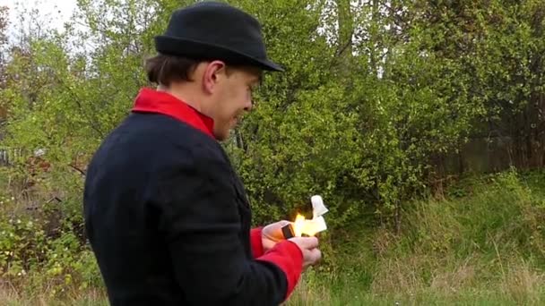 Mann im schwarz-roten Anzug zündet weißes Papier in der Hand an und wirft es in Slo-mo — Stockvideo
