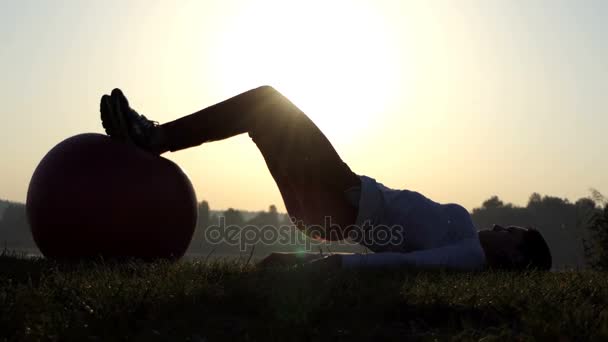 4k Жінка лежить і котиться великий м'яч з ногами на заході сонця . — стокове відео
