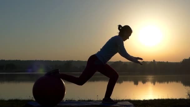 Bir kadın bir koltuk alır ve bir fitball üzerinde tek ayak tutar — Stok video