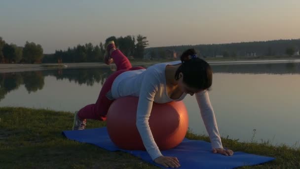 Een slanke vrouw ligt op een fitball en verhoogt haar been — Stockvideo