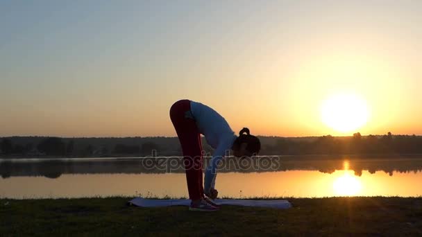 Slim woman bends forward and touches land at sunset — Stock Video