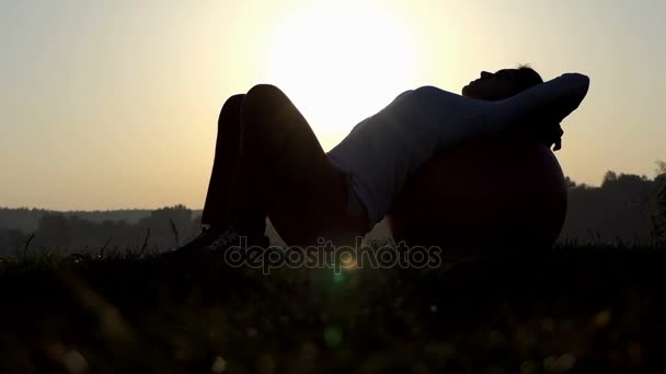 O femeie sportivă o ține din nou pe un fitball și se rostogolește la apusul soarelui. — Videoclip de stoc