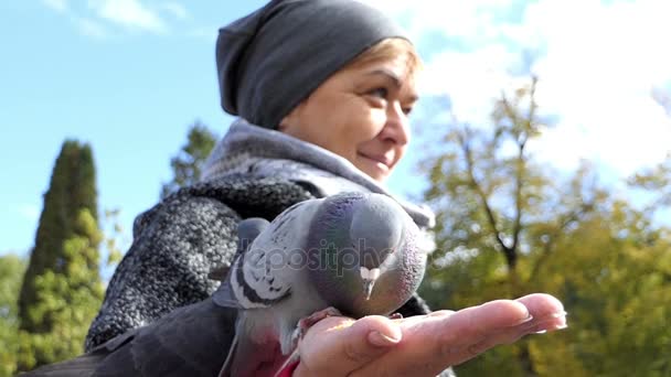 En leende kvinna matar duvor på ett soligt torg i slo-mo — Stockvideo