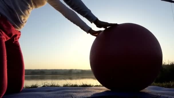 Smal kvinna knäböjer och rullar sin fitball vid solnedgången — Stockvideo