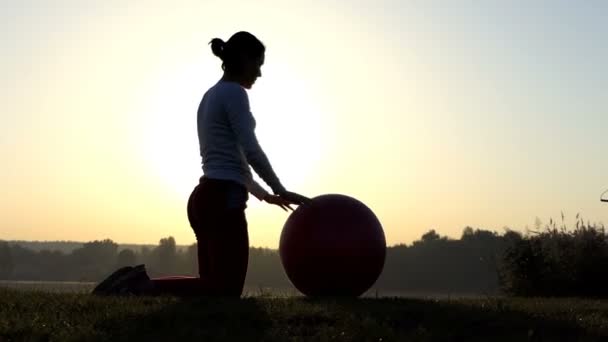 Mulher esportiva se ajoelha e rola seu fitball ao pôr do sol — Vídeo de Stock