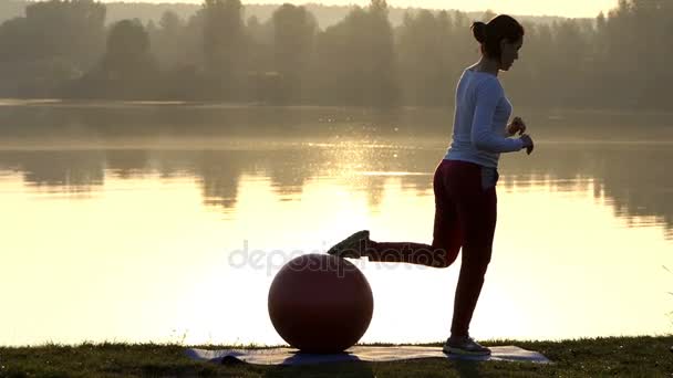 Slim donna mantiene la gamba su un fitball al tramonto — Video Stock