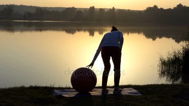 Karcsú nő tartja a kezét a fitball naplementekor — Stock videók