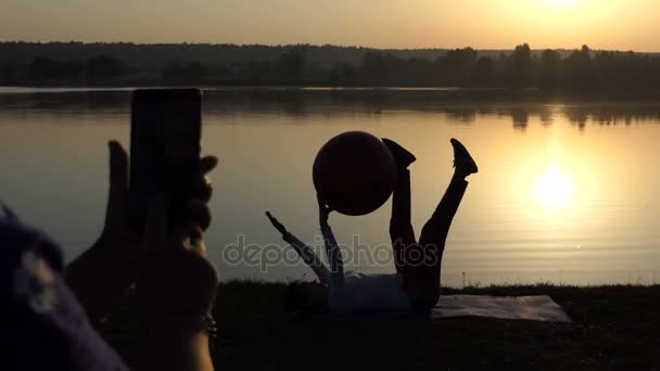Smal kvinna tränar med en fitball, andra skjuter henne — Stockvideo