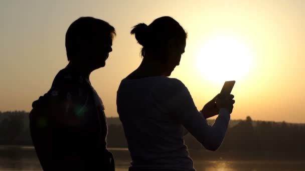 Две женщины смотрят на свой мобильный телефон на берегу озера в сло-мо — стоковое видео