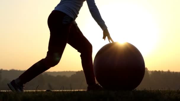 Λεπτή γυναίκα στέκεται, γονατίζει, ρολά της fitball στο ηλιοβασίλεμα — Αρχείο Βίντεο