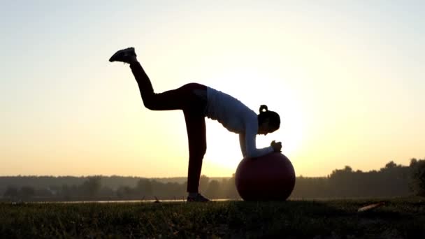 La mujer toca una pelota, mueve su pierna hacia atrás al atardecer — Vídeos de Stock