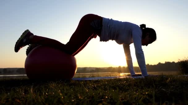 Λεπτή γυναίκα βάζει τα πόδια της σε μια fitball στο ηλιοβασίλεμα σε αργή κίνηση — Αρχείο Βίντεο