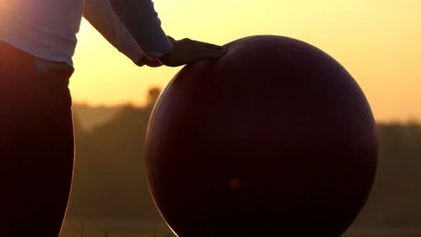 As mãos de mulheres rolam um fitball em um banco de lago no pôr do sol — Vídeo de Stock