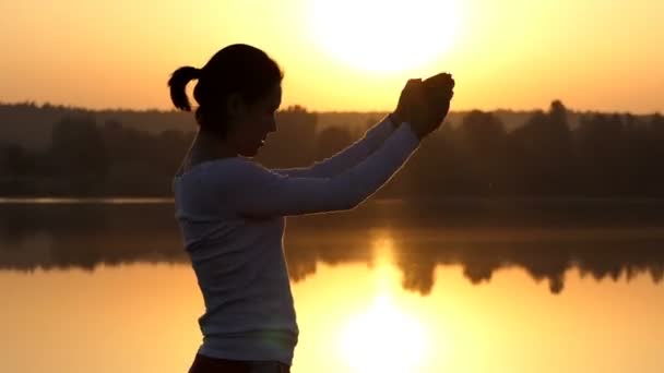 A slim woman rotates her arms and bends at sunset — Stock Video