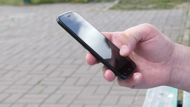 Чоловіча рука торкається екрану мобільного телефону на вулиці — стокове відео