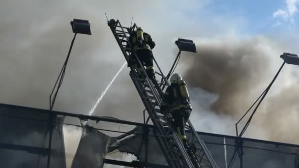 Dos héroes en una escalera metálica apagan el fuego con agua — Vídeo de stock